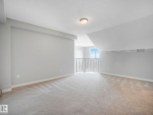 Carpeted loft space featuring light gray walls, a built-in railing with decorative elements, and a sloped ceiling - 2406 320 Clareview Station Drive, Edmonton, AB 