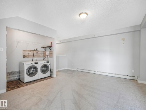 Dedicated laundry area featuring modern appliances, wire shelving, wood-finish accent wall, and wood-finish flooring - 2406 320 Clareview Station Drive, Edmonton, AB 