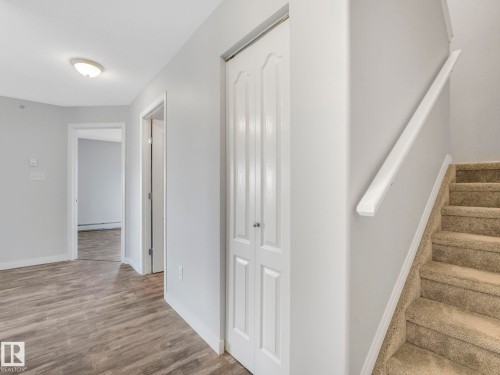 Interior hallway featuring wood-finish flooring, light grey walls, and a carpeted staircase with a white handrail - 2406 320 Clareview Station Drive, Edmonton, AB 