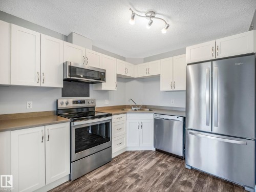 Kitchen featuring white shaker-style cabinetry, stainless steel appliances, wood-finish flooring, and track lighting - 2406 320 Clareview Station Drive, Edmonton, AB 