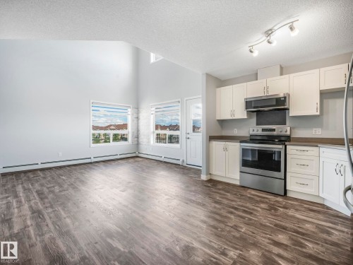 Open-concept living space featuring wood-finish flooring, white cabinetry, stainless steel appliances, a vaulted ceiling, and multiple windows - 2406 320 Clareview Station Drive, Edmonton, AB 