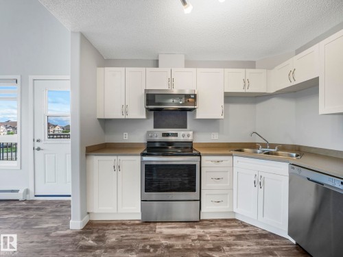 Modern kitchen featuring wood-finish flooring, white cabinetry, and stainless steel appliances including a range, microwave, and dishwasher - 2406 320 Clareview Station Drive, Edmonton, AB 