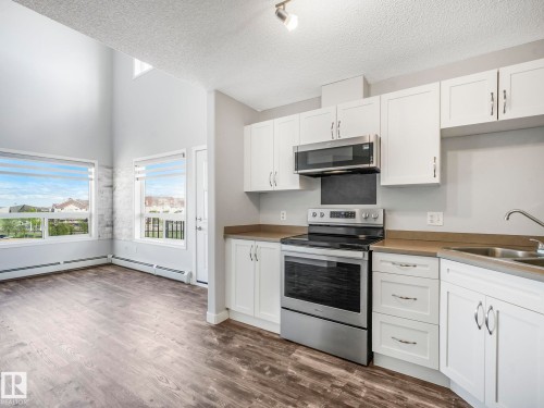 Contemporary kitchen featuring white cabinetry, stainless steel appliances, and a stainless steel sink - 2406 320 Clareview Station Drive, Edmonton, AB 