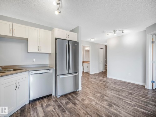 Modern kitchen area featuring stainless steel appliances, white cabinetry, a double basin sink, and wood-finish flooring - 2406 320 Clareview Station Drive, Edmonton, AB 