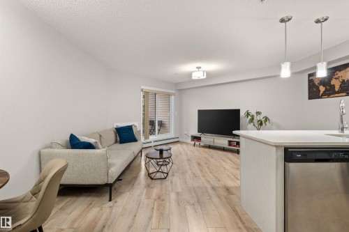 Open-concept living area with wood-finish flooring, a contemporary ceiling light fixture, and a sliding glass door leading to an outdoor space - 210 2229 44 Avenue, Edmonton, AB 