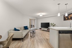 Open-concept living area with wood-finish flooring, a contemporary ceiling light fixture, and a sliding glass door leading to an outdoor space - 