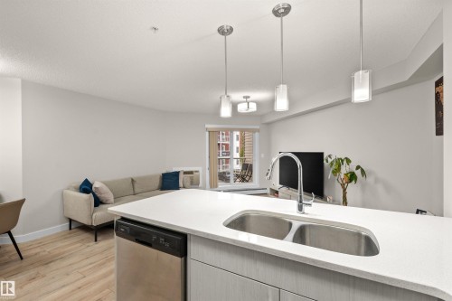 Kitchen island featuring a double basin sink, gooseneck faucet, integrated dishwasher, and light wood-finish cabinetry - 210 2229 44 Avenue, Edmonton, AB 