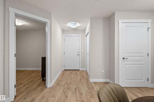 Entryway featuring wood-finish flooring, light neutral wall tones, white trim, and white panel doors with brushed nickel hardware - 210 2229 44 Avenue, Edmonton, AB 