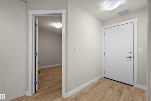 Entryway featuring wood-finish flooring, white trim, a solid-core door with contemporary hardware, and a semi-flush ceiling light fixture - 210 2229 44 Avenue, Edmonton, AB 