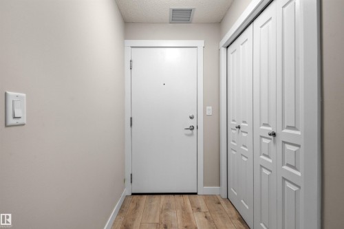 Entryway featuring wood-finish flooring, a white paneled door, and built-in bifold closet doors with polished hardware - 210 2229 44 Avenue, Edmonton, AB 