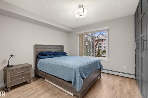 Bedroom with light wood-finish flooring, a large window, a ceiling-mounted light fixture, and built-in panel-front cabinetry - 210 2229 44 Avenue, Edmonton, AB 