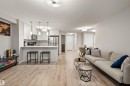 Open-concept living space featuring wood-finish flooring, a contemporary kitchen with white cabinetry and stainless steel appliances, a kitchen island with seating, pendant lighting, and recessed ceiling lights - 210 2229 44 Avenue, Edmonton, AB 