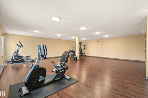 Spacious fitness area featuring wood-finish flooring, ample overhead lighting, and neutral wall tones - 210 2229 44 Avenue, Edmonton, AB 