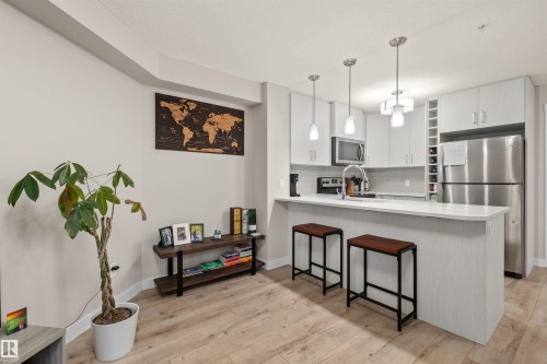 Modern kitchen featuring light-toned cabinetry, stainless steel appliances, a white subway tile backsplash, and a breakfast bar with pendant lighting - 210 2229 44 Avenue, Edmonton, AB 