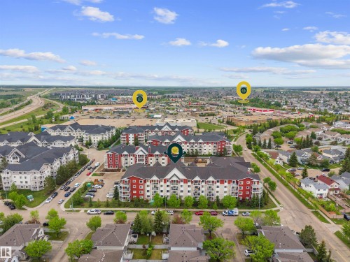 Aerial perspective showcasing a multi-story residential building with red and beige siding, white balconies, and dark roofing - 210 2229 44 Avenue, Edmonton, AB 