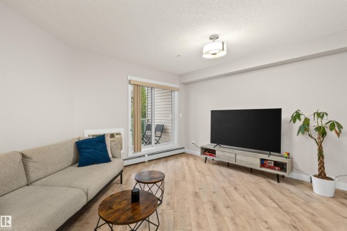 Living area featuring wood-finish flooring, a neutral color palette, and a sliding glass door opening to a private balcony - 210 2229 44 Avenue, Edmonton, AB 