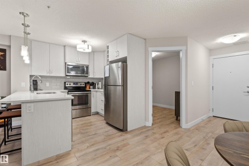Kitchen featuring light wood-finish flooring, white cabinetry, stainless steel appliances, a white countertop island, and a subway tile backsplash - 210 2229 44 Avenue, Edmonton, AB 