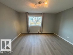Spacious room featuring light wood-finish flooring, neutral gray walls, a large window, and a three-bulb track light fixture - 