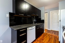 Kitchen featuring dark cabinetry with silver-tone hardware, a black solid surface backsplash, a stainless steel sink with a high-arc faucet, and granite countertops - 