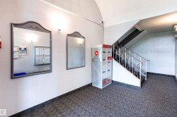 Carpeted entryway featuring a staircase with a decorative metal railing, two framed mirrors, and wall-mounted lighting fixtures - 