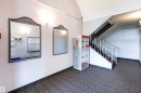 Carpeted entryway featuring a staircase with a decorative metal railing, two framed mirrors, and wall-mounted lighting fixtures - 202 10740 105 Street, Edmonton, AB 