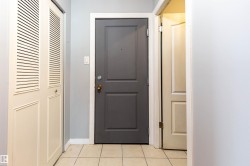 Entryway featuring a dark gray paneled door with brass hardware, light blue painted walls, white baseboards, and square tile flooring - 