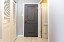 Entryway featuring a dark gray paneled door with brass hardware, light blue painted walls, white baseboards, and square tile flooring - 202 10740 105 Street, Edmonton, AB 