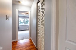 Hallway with wood-finish flooring, a white louvered bifold closet door, and light gray painted walls - 