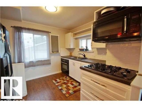 Kitchen featuring a built-in black cooktop, white cabinetry with bronze-finish hardware, dark countertops, and wood-finish flooring - 9815 160 Street, Edmonton, AB 