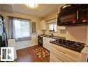 Kitchen featuring a built-in black cooktop, white cabinetry with bronze-finish hardware, dark countertops, and wood-finish flooring - 9815 160 Street, Edmonton, AB 
