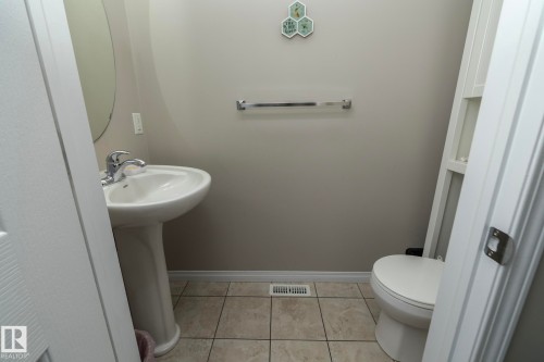 Pedestal sink with chrome faucet, complemented by a round mirror, tile flooring, and a white toilet - 46 4050 Savaryn Drive, Edmonton, AB 