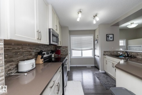 Contemporary kitchen featuring white cabinetry, a mosaic tile backsplash, dark wood-finish flooring, and recessed lighting - 46 4050 Savaryn Drive, Edmonton, AB 