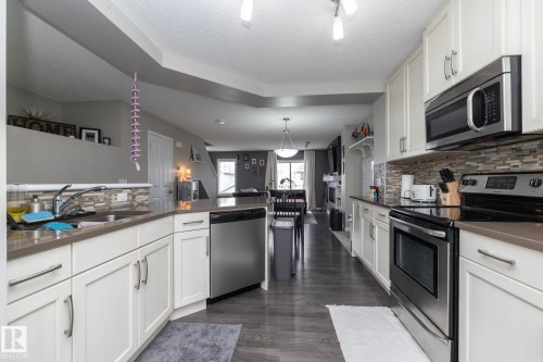 Kitchen featuring white shaker-style cabinetry, stainless steel appliances, dark wood-finish flooring, and light-toned countertops with a mosaic tile backsplash - 46 4050 Savaryn Drive, Edmonton, AB 