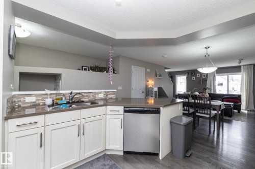 Kitchen featuring white cabinetry, a stainless steel dishwasher, and a multi-tone tile backsplash - 46 4050 Savaryn Drive, Edmonton, AB 