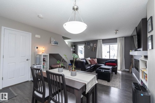 Open concept living area featuring dark wood-finish flooring, a contemporary ceiling light fixture, a built-in fireplace with a white mantel, and a sliding glass door - 46 4050 Savaryn Drive, Edmonton, AB 