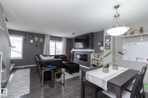 Open-concept living area featuring wood-finish flooring, a contemporary fireplace with a built-in media center, and a dining area with a modern chandelier - 46 4050 Savaryn Drive, Edmonton, AB 