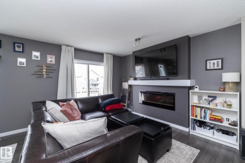Living area featuring a modern linear electric fireplace with a white mantel, dark wood-finish flooring, and a large sliding glass door - 46 4050 Savaryn Drive, Edmonton, AB 
