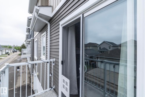 Balcony with white metal railing, featuring a large glass sliding door and gray horizontal siding - 46 4050 Savaryn Drive, Edmonton, AB 