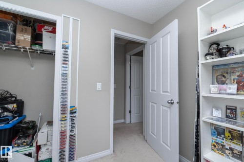 Interior hallway featuring a closet with wire shelving, carpet flooring, a built-in white bookshelf, and an interior door with a silver-tone knob - 46 4050 Savaryn Drive, Edmonton, AB 