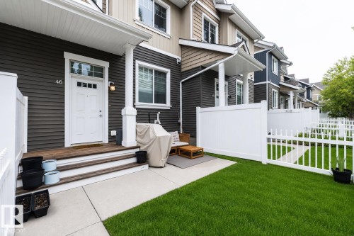Contemporary townhome exterior featuring dark gray siding, a white entry door with transom window, and a covered porch - 46 4050 Savaryn Drive, Edmonton, AB 