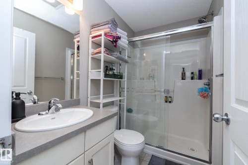 Bathroom featuring a white shower with glass enclosure, white toilet, single vanity with integrated sink, and a mirrored wall - 46 4050 Savaryn Drive, Edmonton, AB 