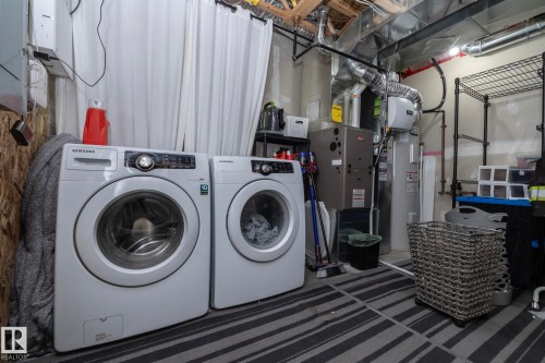 Dedicated laundry area featuring a front-loading washer and dryer, exposed ceiling joists, utility shelving, and a water heater - 46 4050 Savaryn Drive, Edmonton, AB 