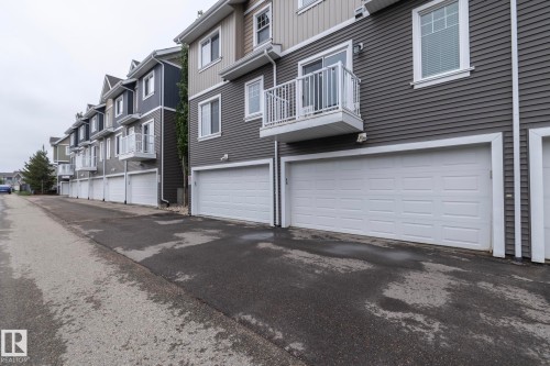 Modern townhome exterior featuring multi-toned siding, a panel garage door, a white-railed balcony, and white-framed windows - 46 4050 Savaryn Drive, Edmonton, AB 