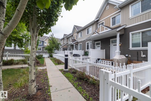 Row of residential townhomes featuring multi-toned siding, white trim, and individual front patios with white picket fencing - 46 4050 Savaryn Drive, Edmonton, AB 