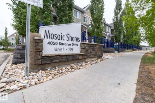 Stone-clad monument sign with raised lettering, surrounded by decorative river rock landscaping - 46 4050 Savaryn Drive, Edmonton, AB 