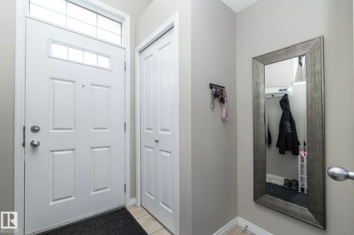 Entryway featuring a paneled door with transom window, bifold closet doors, light neutral wall paint, and tile flooring - 46 4050 Savaryn Drive, Edmonton, AB 