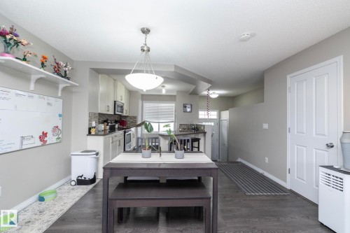 Open-concept living area featuring dark wood-finish flooring, a contemporary dining fixture, and kitchen with light cabinetry, dark countertops, and stainless steel appliances - 46 4050 Savaryn Drive, Edmonton, AB 