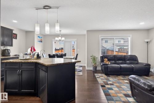 Open-concept living area featuring rich wood-finish flooring, a kitchen island with a light-toned countertop, dark cabinetry, and recessed lighting - 3350 18B Street, Edmonton, AB 