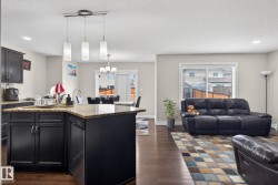 Open-concept living area featuring rich wood-finish flooring, a kitchen island with a light-toned countertop, dark cabinetry, and recessed lighting - 