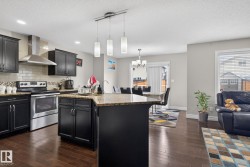 Open-concept kitchen with dark wood-finish cabinetry, stainless steel appliances, a multi-tonal backsplash, and an island with a light-toned countertop - 